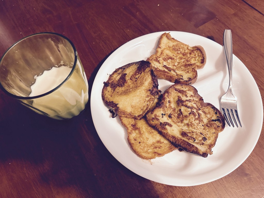 Photo of a plate with french toast and a cup of oat milk.