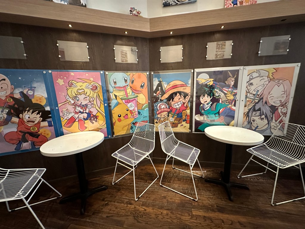 Photo of the inside of the cafe. Anime posters on the wall near a seating area.